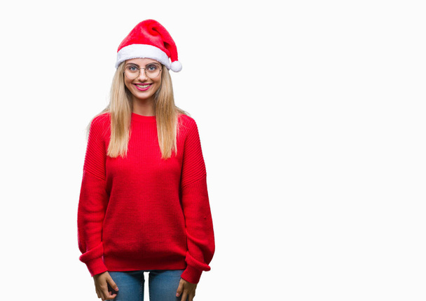 Νέοι όμορφη ξανθιά γυναίκα που φοράει καπέλο Χριστουγέννων πέρα από το απομονωμένο υπόβαθρο με ένα ευτυχισμένο και δροσερό χαμόγελο στο πρόσωπο. Τυχερό πρόσωπο. - Φωτογραφία, εικόνα