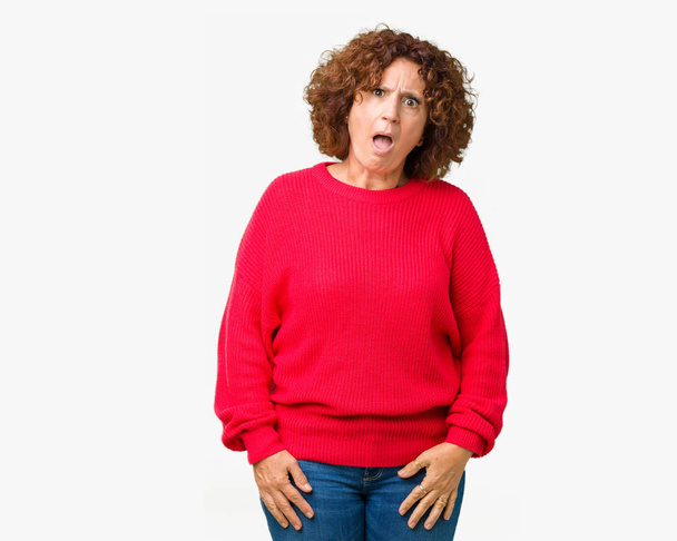 Beautiful middle ager senior woman red winter sweater over isolated background In shock face, looking skeptical and sarcastic, surprised with open mouth - Foto, Imagem
