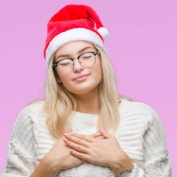 Young caucasian woman wearing christmas hat over isolated background smiling with hands on chest with closed eyes and grateful gesture on face. Health concept. - Foto, immagini