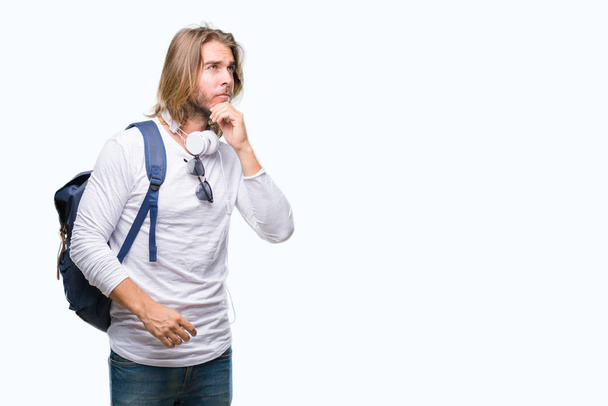 Mladý pohledný turistický muž s dlouhými vlasy nosit batoh izolované pozadí s rukou na bradě přemýšlet o otázce, zamyšlený výraz. Usmívající se zamyšlenou tváři. Pochybnost koncept. - Fotografie, Obrázek