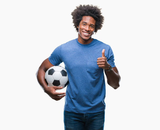 Afro american man holding football ball over isolated background happy with big smile doing ok sign, thumb up with fingers, excellent sign - 写真・画像