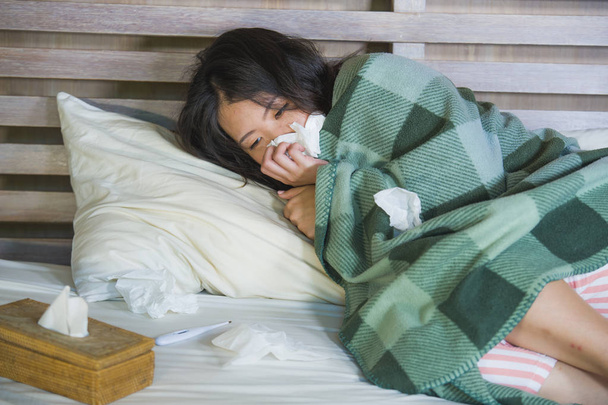 young sick sweet Asian Chinese woman in pajamas covered with blanket lying feverish on bed suffering cold and flu in medical health care and influenza virus disease concept - Photo, image