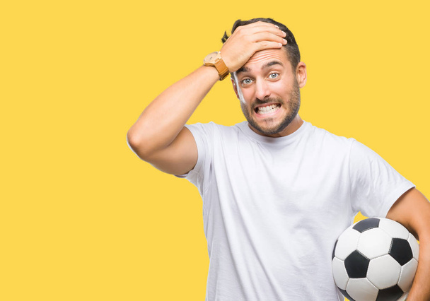 サッカー サッカー ボールの頭の上の手を強調した分離の背景の上に保持している若いハンサムな男は恥と驚きの顔でショックを受けて怒っているとイライラします。恐怖と動揺の間違い. - 写真・画像