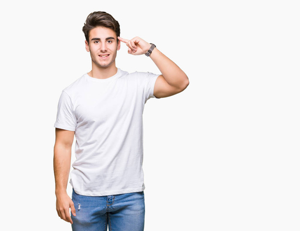 Nuori komea mies yllään valkoinen t-paita yli eristetty tausta Hymyilevä osoittaa päähän yhdellä sormella, hyvä idea tai ajatus, hyvä muisti
 - Valokuva, kuva