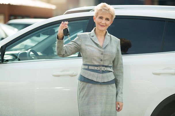stylish woman in age, in a suit standing near a car in the summer with keys in hands - Фото, зображення
