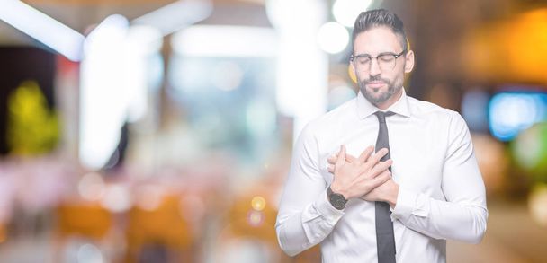 Young handsome business man wearing glasses over isolated background smiling with hands on chest with closed eyes and grateful gesture on face. Health concept. - Fotoğraf, Görsel