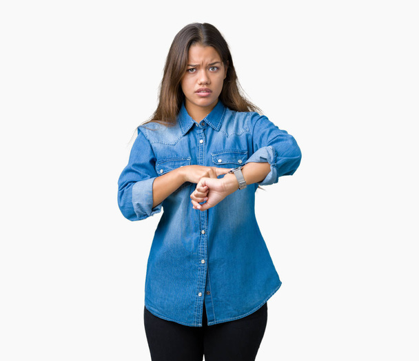 Young beautiful brunette woman wearing blue denim shirt over isolated background In hurry pointing to watch time, impatience, upset and angry for deadline delay - Photo, Image