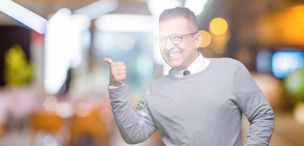 Empresarios de mediana edad árabe hombre con gafas sobre fondo aislado sonriendo con la cara feliz mirando y señalando a un lado con el pulgar hacia arriba
. - Foto, imagen