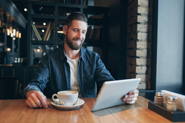 Young man drinking coffee in cafe and using tablet computer - Photo, Image
