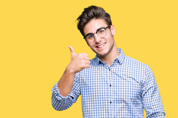 Mladý pohledný muž nosí brýle izolované pozadí dělá šťastné palec nahoru gesto rukou. Schvalování výraz s ukazuje úspěch při pohledu na fotoaparát. - Fotografie, Obrázek