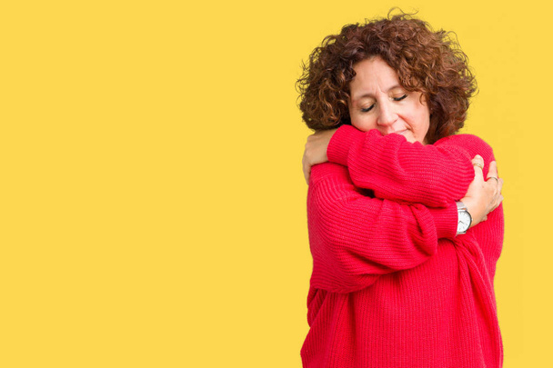 Пожилая женщина средних лет в красном зимнем свитере на обособленном фоне обнимает себя, счастлива и позитивна, улыбается уверенно. Самолюбие и забота о себе
 - Фото, изображение