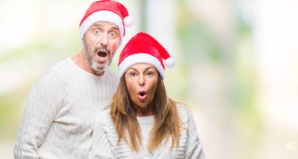 Középkorú hispán pár visel karácsonyi kalap elszigetelt háttér, félek, és Megdöbbentem, meglepetés kifejezés, mint a félelem, és arca izgatott. - Fotó, kép
