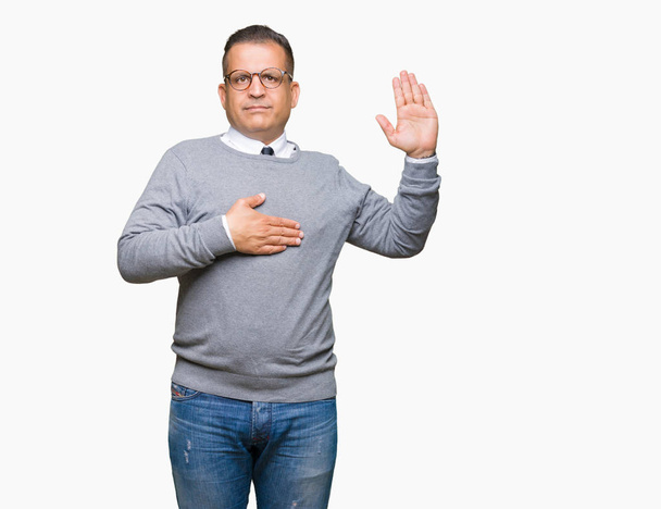 arabischer Mann mittleren Alters mit Brille vor isoliertem Hintergrund, der mit der Hand auf der Brust und offener Handfläche flucht und einen Treueschwur ablegt - Foto, Bild