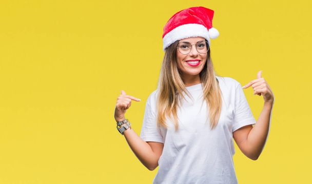 若くてきれいな女性の顔に笑顔と自信を持って、誇りと幸せな指で自分を指している孤立した背景にクリスマスの帽子をかぶって. - 写真・画像