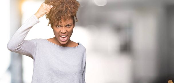Beautiful young african american woman over isolated background angry and mad raising fist frustrated and furious while shouting with anger. Rage and aggressive concept. - Photo, Image