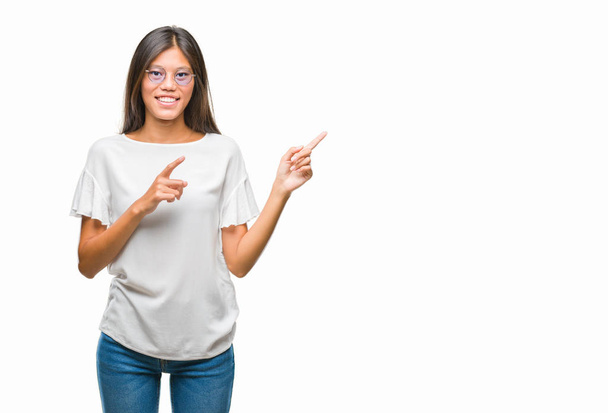 Giovane donna asiatica indossa occhiali su sfondo isolato sorridente e guardando la fotocamera che punta con due mani e le dita di lato
. - Foto, immagini