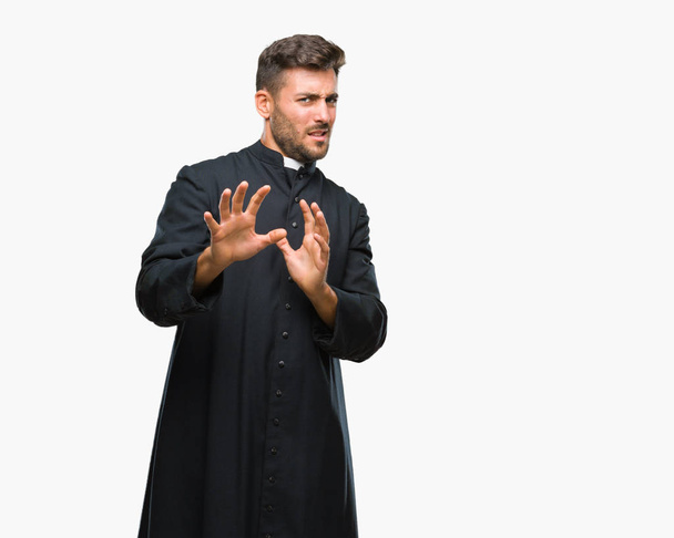 Young catholic christian priest man over isolated background disgusted expression, displeased and fearful doing disgust face because aversion reaction. With hands raised. Annoying concept. - Foto, Bild