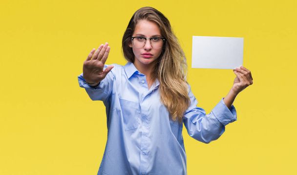 Jonge mooie blonde vrouw bedrijf leeg visitekaartje op geïsoleerde achtergrond met open hand doen stopbord met ernstige en vol vertrouwen meningsuiting, defensie gebaar - Foto, afbeelding