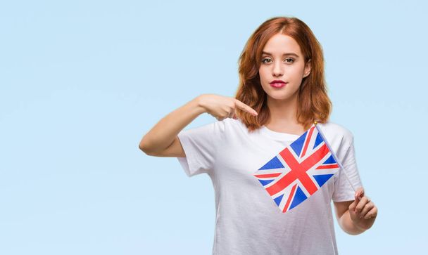 Молодая красивая женщина с флагом Соединенного Королевства на изолированном фоне с неожиданным лицом, указывающим пальцем на себя
 - Фото, изображение