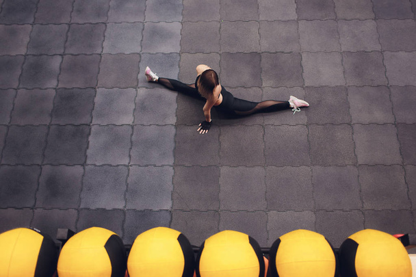 Top view of a fit and sporty girl doing streching exercises for legs. Young slim woman doing twine in the gym, stadium. Indoors. - Foto, Bild