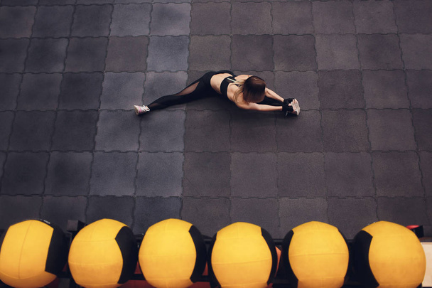 Top view of a fit and sporty girl doing streching exercises for legs. Young slim woman doing twine in the gym, stadium. Indoors. - Fotografie, Obrázek