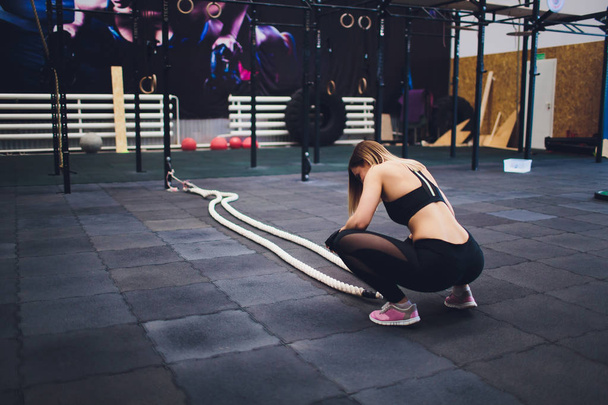 Strong woman exercising with battle ropes at the gym. Athlete doing battle rope workout at gym. woman tired to train. - Fotó, kép