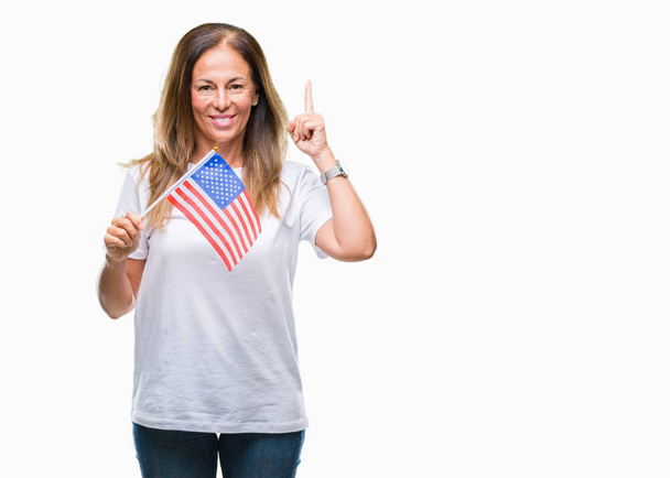 Middle age hispanic woman holding flag of United States of America over isolated background surprised with an idea or question pointing finger with happy face, number one - 写真・画像