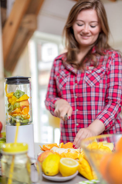 Young smiling woman making smoothie with fresh greens in the blender in kitchen at home. - Fotoğraf, Görsel