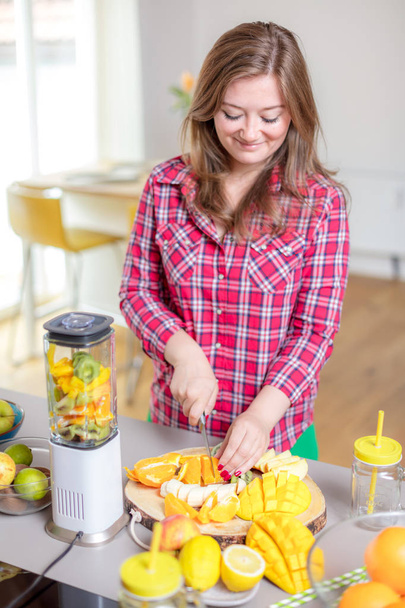 Young smiling woman making smoothie with fresh greens in the blender in kitchen at home. - Foto, imagen