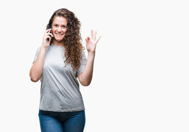 Jeune fille brune parlant sur smartphone sur fond isolé faisant ok signe avec les doigts, excellent symbole
 - Photo, image