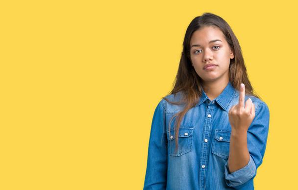 Young beautiful brunette woman wearing blue denim shirt over isolated background Showing middle finger, impolite and rude fuck off expression - Photo, Image
