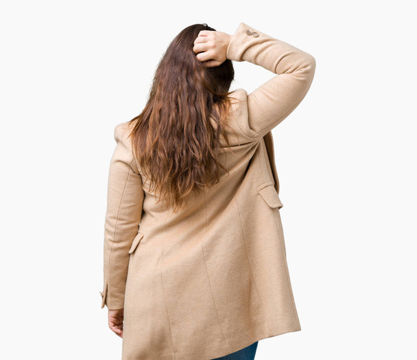 Beautiful plus size young woman wearing winter coat over isolated background Backwards thinking about doubt with hand on head - Φωτογραφία, εικόνα
