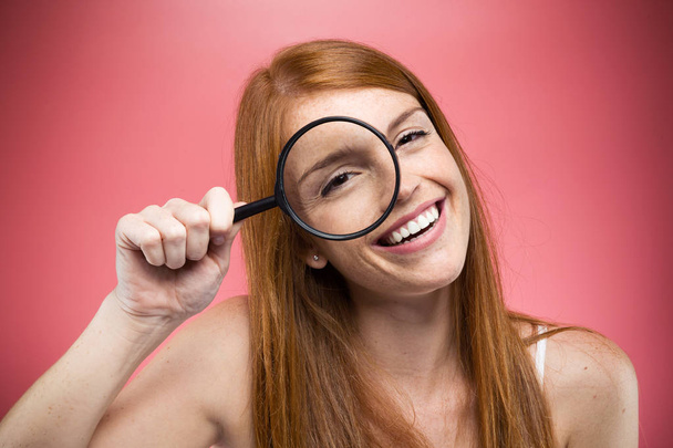 Portrait of cheerful pretty girl looking through magnifying glass isolated over pink background - Photo, Image