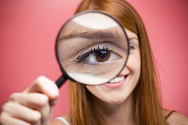 Portrait of cheerful pretty girl looking through magnifying glass isolated over pink background - Photo, Image