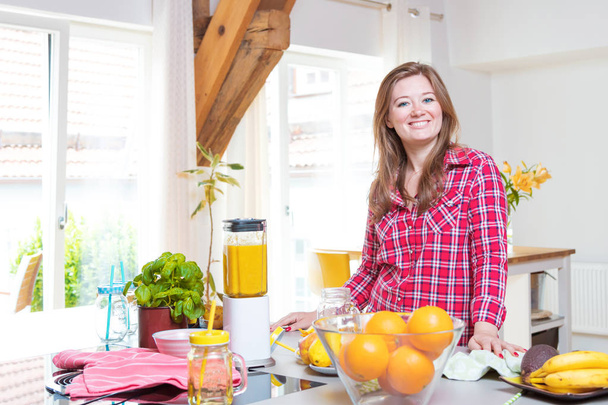 Fiatal mosolygó nő, ami smoothie, friss zöldséggel, a turmixgépben otthon a konyhában. - Fotó, kép