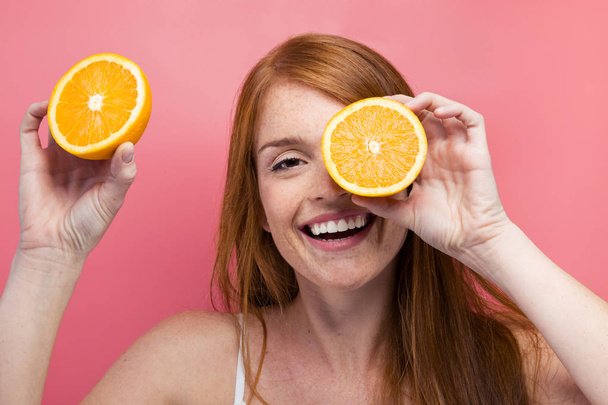 Portrait of funny young woman holding orange slices at her face and looking at camera over pink background. - Φωτογραφία, εικόνα