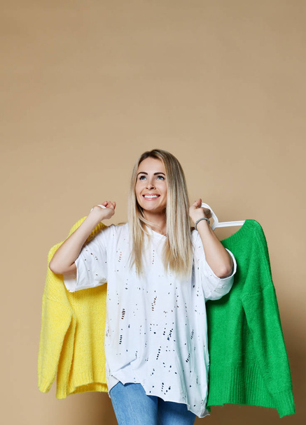 Woman shopping Christmas sale choose between two sweaters blouse green and yellow happy smiling  - Photo, Image