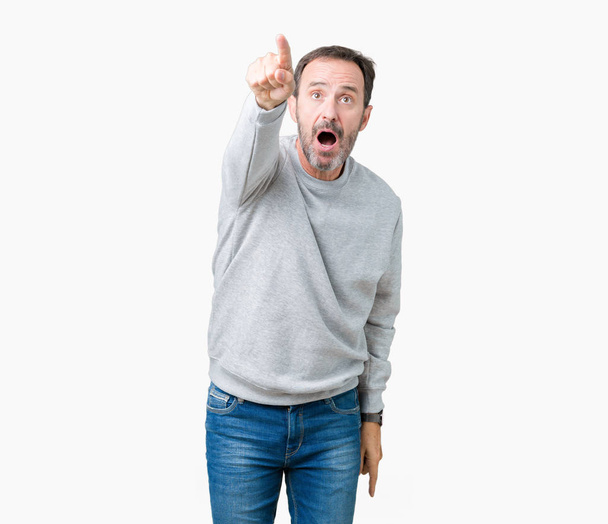 Handsome middle age senior man wearing a sweatshirt over isolated background Pointing with finger surprised ahead, open mouth amazed expression, something in front - Foto, Bild