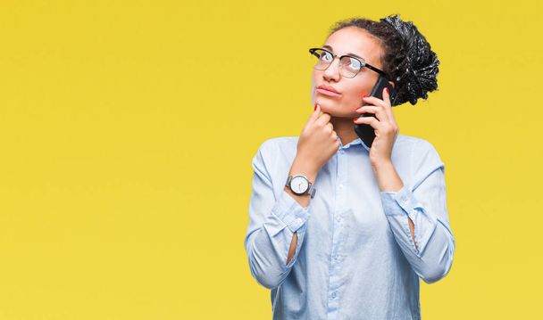 Young braided hair african american business girl showing calling using smartphone over isolated background serious face thinking about question, very confused idea - Foto, immagini