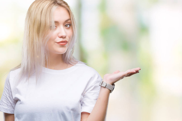 Jeune femme blonde sur fond isolé souriant gai présentation et pointant avec la paume de la main en regardant la caméra
. - Photo, image