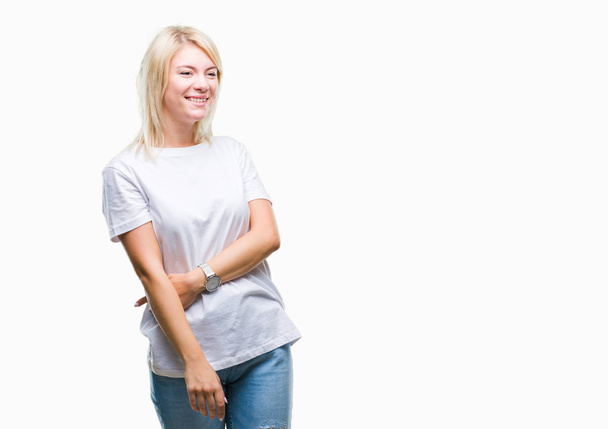 Young beautiful blonde woman wearing white t-shirt over isolated background looking away to side with smile on face, natural expression. Laughing confident. - Photo, Image