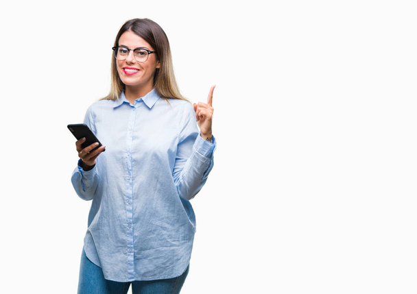 junge schöne Geschäftsfrau SMS mit Smartphone über isolierten Hintergrund sehr glücklich zeigt mit der Hand und dem Finger zur Seite - Foto, Bild