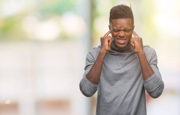 Jovem afro-americano sobre fundo isolado cobrindo orelhas com dedos com expressão irritada para o ruído da música alta. Conceito de surdo
. - Foto, Imagem