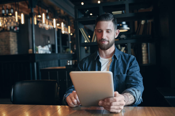 Современный хипстерский бизнесмен пьет кофе в городском кафе во время обеда и работает на планшете
 - Фото, изображение