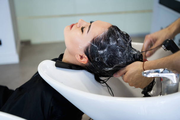 Salon fryzjerski. Kobieta siedzieć podczas mycia włosów w salonie. - Zdjęcie, obraz