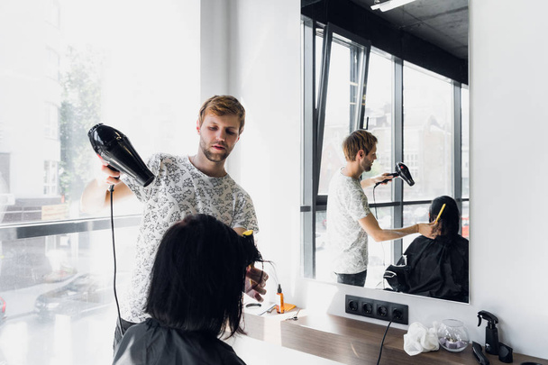 Мужчина парикмахер улыбается и разговаривает с клиентом, делая новую стрижку для красивой молодой брюнетки
 - Фото, изображение