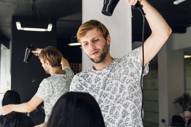 Professional smiling male stylist blow drying womans hair with a dryer in salon - Photo, Image