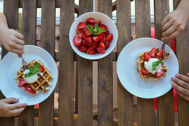 Two boys eat for Breakfast Viennese waffles with ice cream and strawberries. Top view. - Фото, изображение