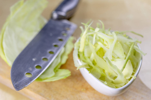Fresh white cabbage cut into strips on the kitchen table. Vegetables prepared for salad. Light background. - Foto, Imagen