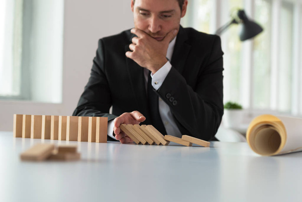 Huolestunut vakava liikemies istuu pöytänsä ääressä pysäyttäen dominoefektin kädellään suunnitellessaan yhtiönsä tulevaisuutta.
. - Valokuva, kuva